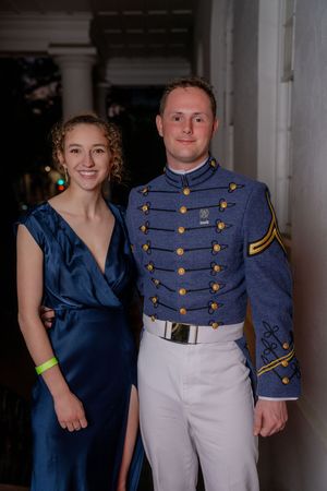 Military cadet in dress uniform with gold buttons and white pants poses with companion in navy blue formal dress.