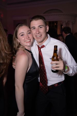 A couple in formal attire smiles and poses together at what appears to be a dance or party event.