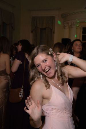 Person in a light pink dress dances enthusiastically at an indoor event.