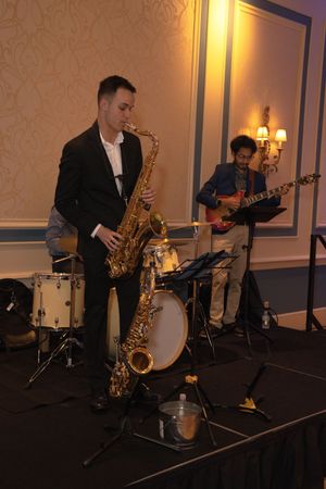 Jazz musicians perform on stage with saxophone, guitar, and drums in an elegant venue with warm lighting.