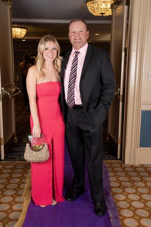 Elegantly dressed couple posing at a formal event with patterned carpet and crystal chandeliers.