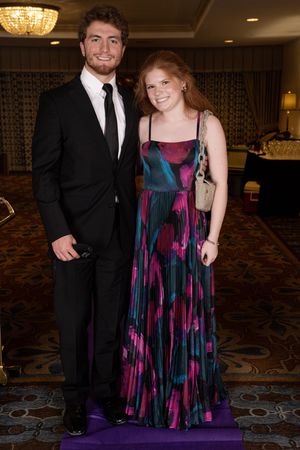 Formal pair posing at event with one wearing colorful flowing dress with pink and blue pattern.