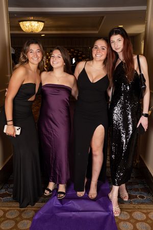 A group poses together at a formal event wearing black and purple evening dresses.