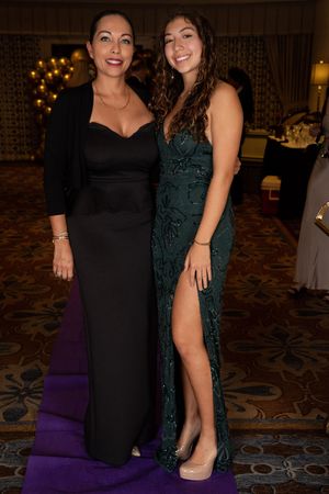 Two women in formal dresses pose together at an evening event with elegant lighting and decor.