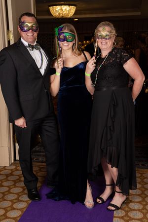 Guests in formal black attire and decorative masks pose together at an elegant masquerade ball event.