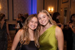 Two smiling friends pose together at an evening event, with one wearing a black top and one in a lime green dress.