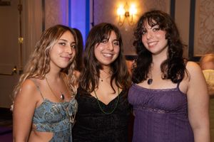Three friends pose together at an elegant event, wearing formal dresses in blue, black and purple.