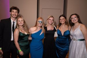 A group of people wearing formal attire pose together at a social gathering in a dimly lit room.