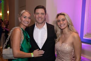 A group of people in formal attire pose together at an event with purple lighting and decor.