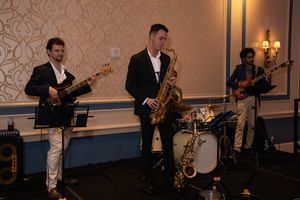 Musicians perform with instruments on stage at an elegant venue with warm lighting and patterned walls.