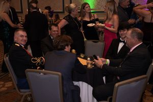 People gathered in formal attire at an elegant indoor event with tables and chairs.