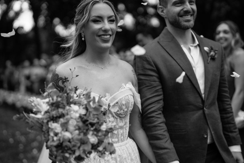 A joyful wedding couple shares a candid moment together while holding a rustic floral bouquet in an outdoor setting.