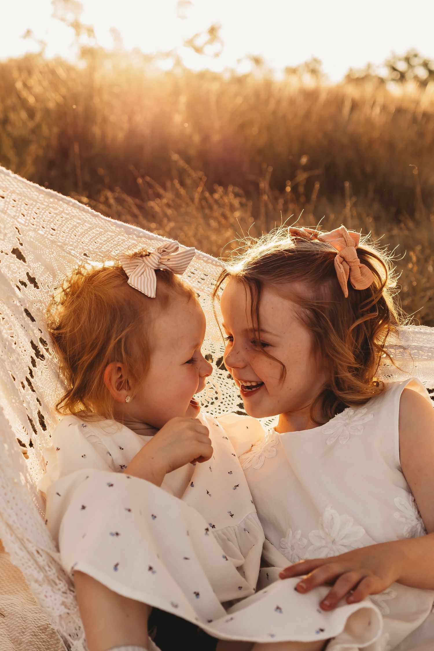 Two children laying on a blanket outdoors share joyful moments together in warm sunset lighting.