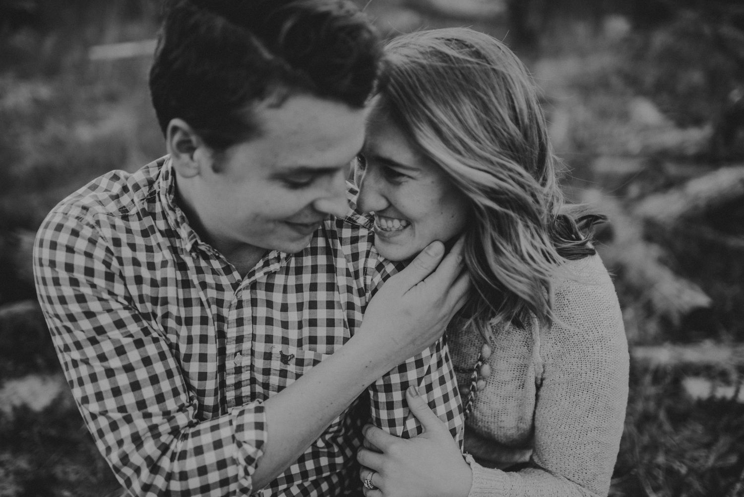 Black and white photo of a couple sharing a tender, laughing moment during an engagement shoot.