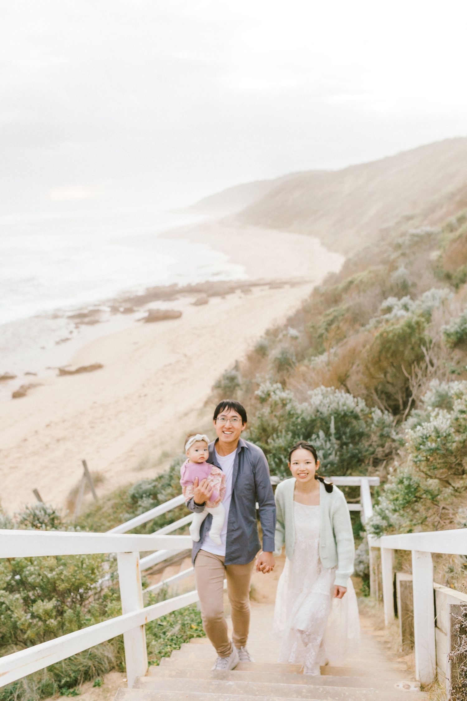 A family walks along a scenic coastal path with white fencing and sandy cliffs in the background.