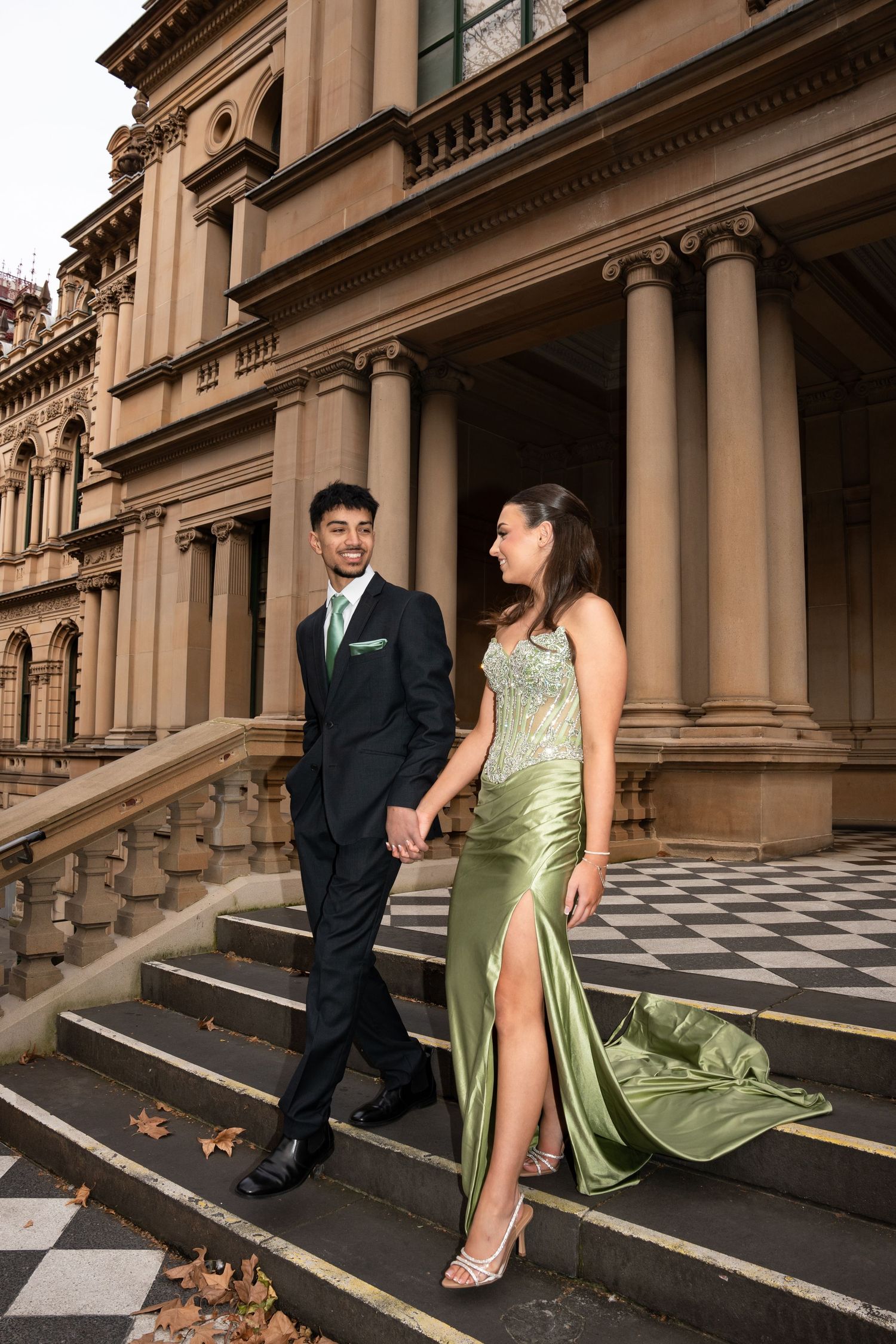Formal couple in suit and green silk gown posing on ornate historic building steps.