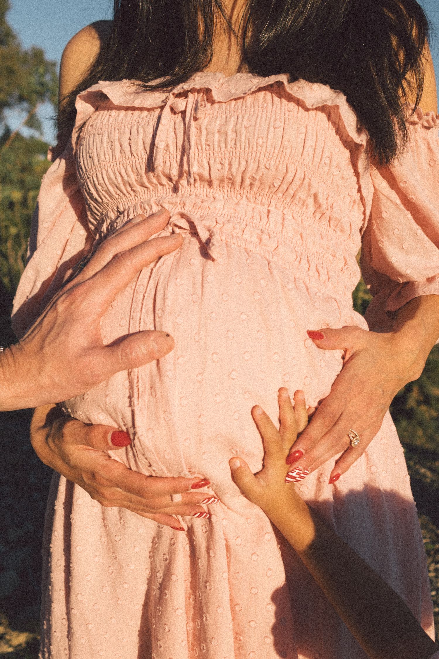 A person wearing a peach-colored dress holds their pregnant belly in a series of outdoor maternity photos at sunset.