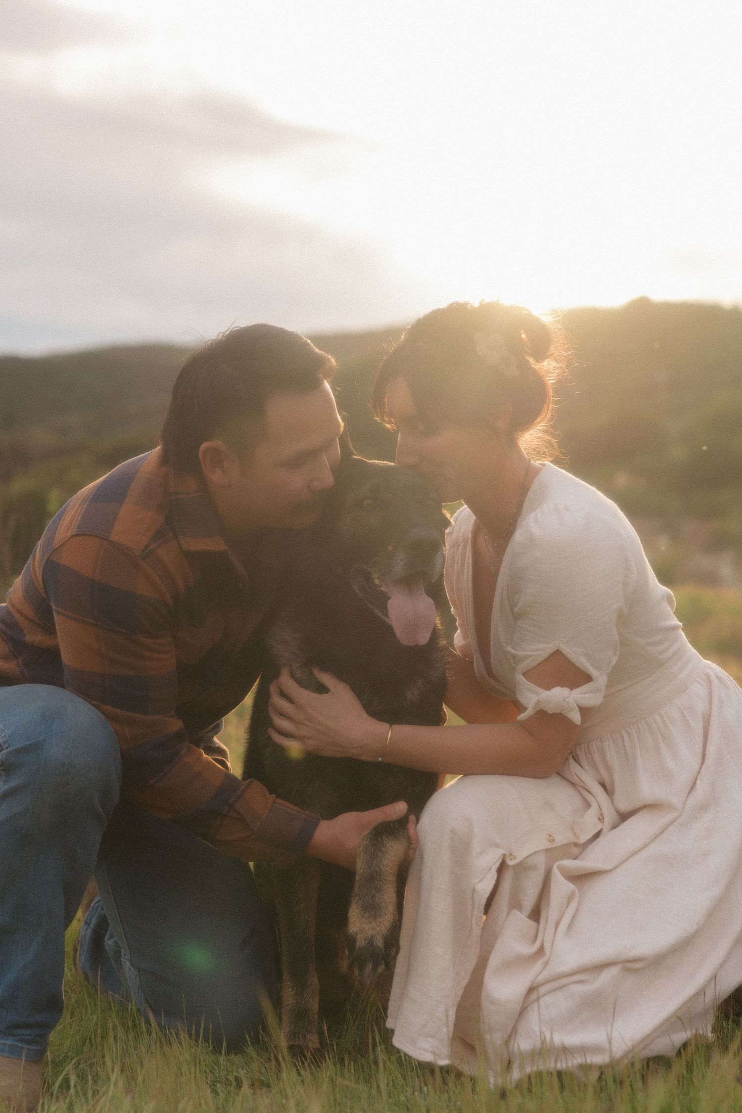 A couple sits together in a grassy field during golden hour as sunlight creates a romantic silhouette.