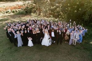 Large wedding party group photo taken outdoors with trees in the background.