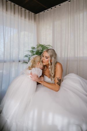 A flowing white wedding dress spreads across a light-colored couch in an indoor setting.