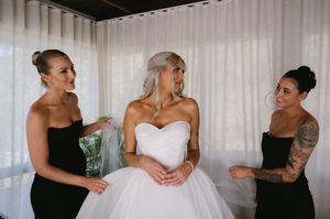 Three people in formal attire gather together, with a central figure wearing a stunning white strapless wedding gown.