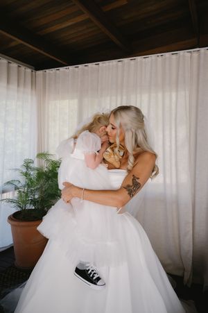 A tender moment in white featuring a flowing wedding dress and casual black sneakers against sheer curtains.