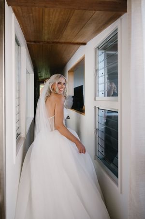 Bride in a voluminous white gown walks through a bright hallway with wooden ceiling.