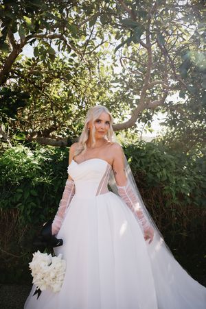 A bride in a strapless wedding gown poses in a garden setting with greenery.