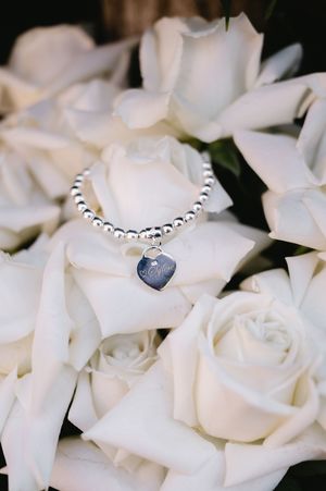 A silver beaded bracelet with heart charm nestled among white roses in a bridal bouquet.