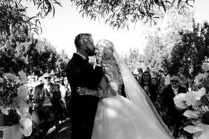 A black and white photo captures a romantic moment during an outdoor wedding ceremony.