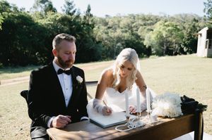 Wedding party sits at an outdoor table signing documents during a sunny afternoon ceremony.