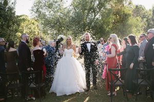 Newlyweds walking down the aisle while guests shower them with confetti in an outdoor setting.