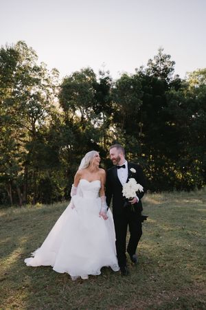 Newlyweds walk together across a grassy hillside during their wedding photo session.