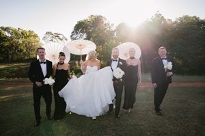 Wedding party walks together across a grassy field at golden hour with sunlight streaming through trees.