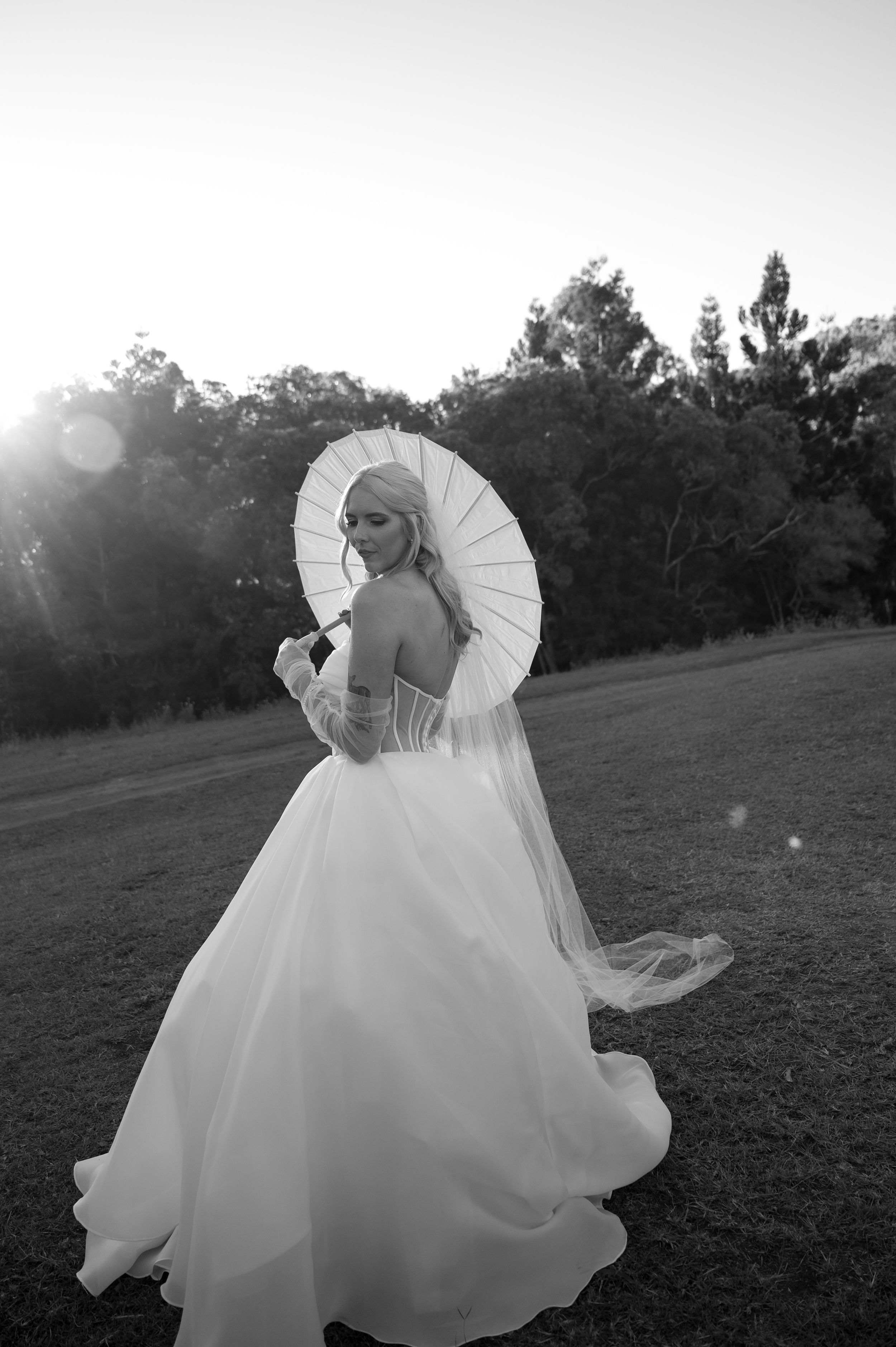 Bride with parasol twirls in her gown during sunset outdoor photoshoot.