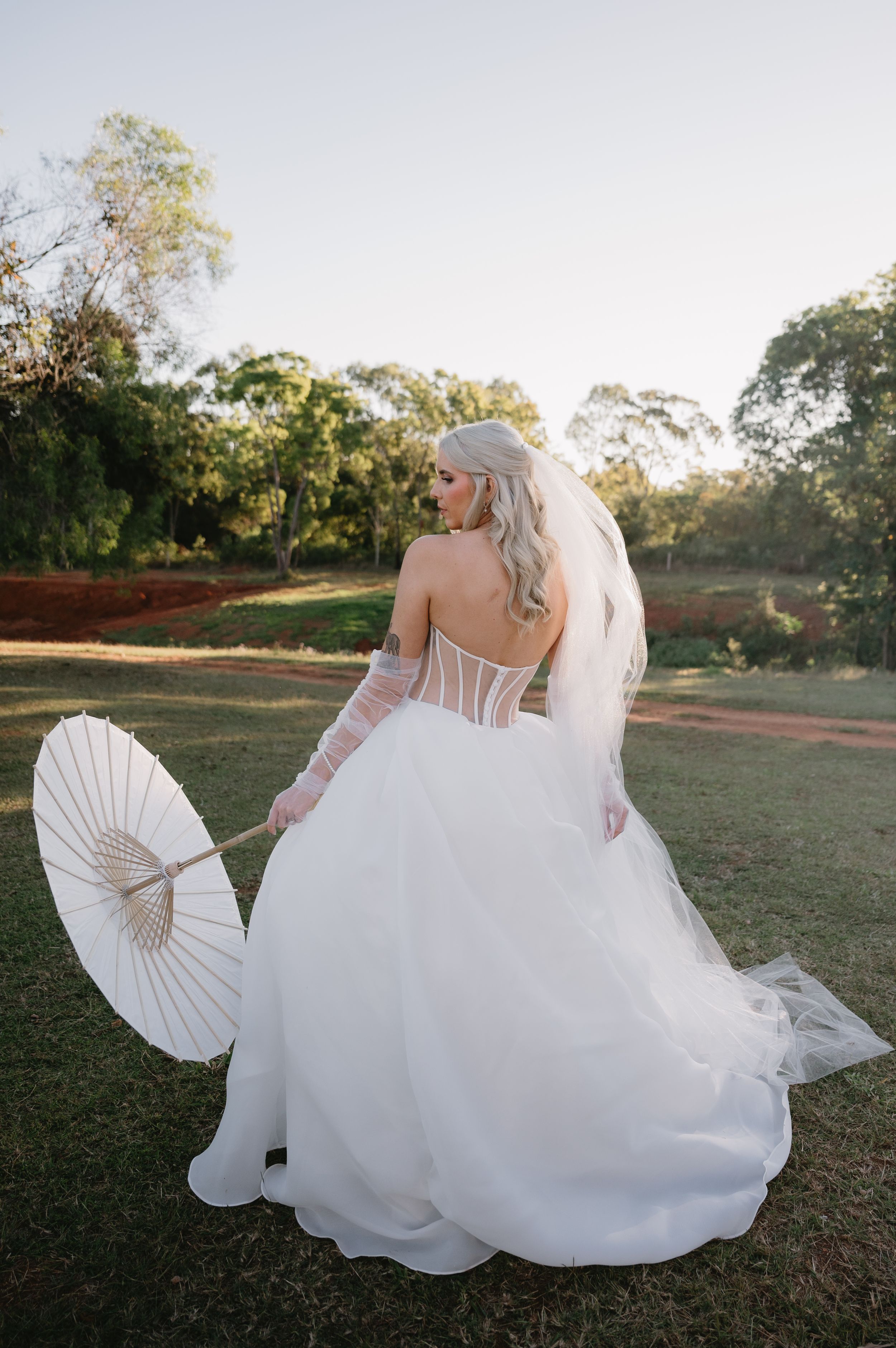 A bride in a flowing white wedding dress twirls gracefully on a grassy lawn at sunset.