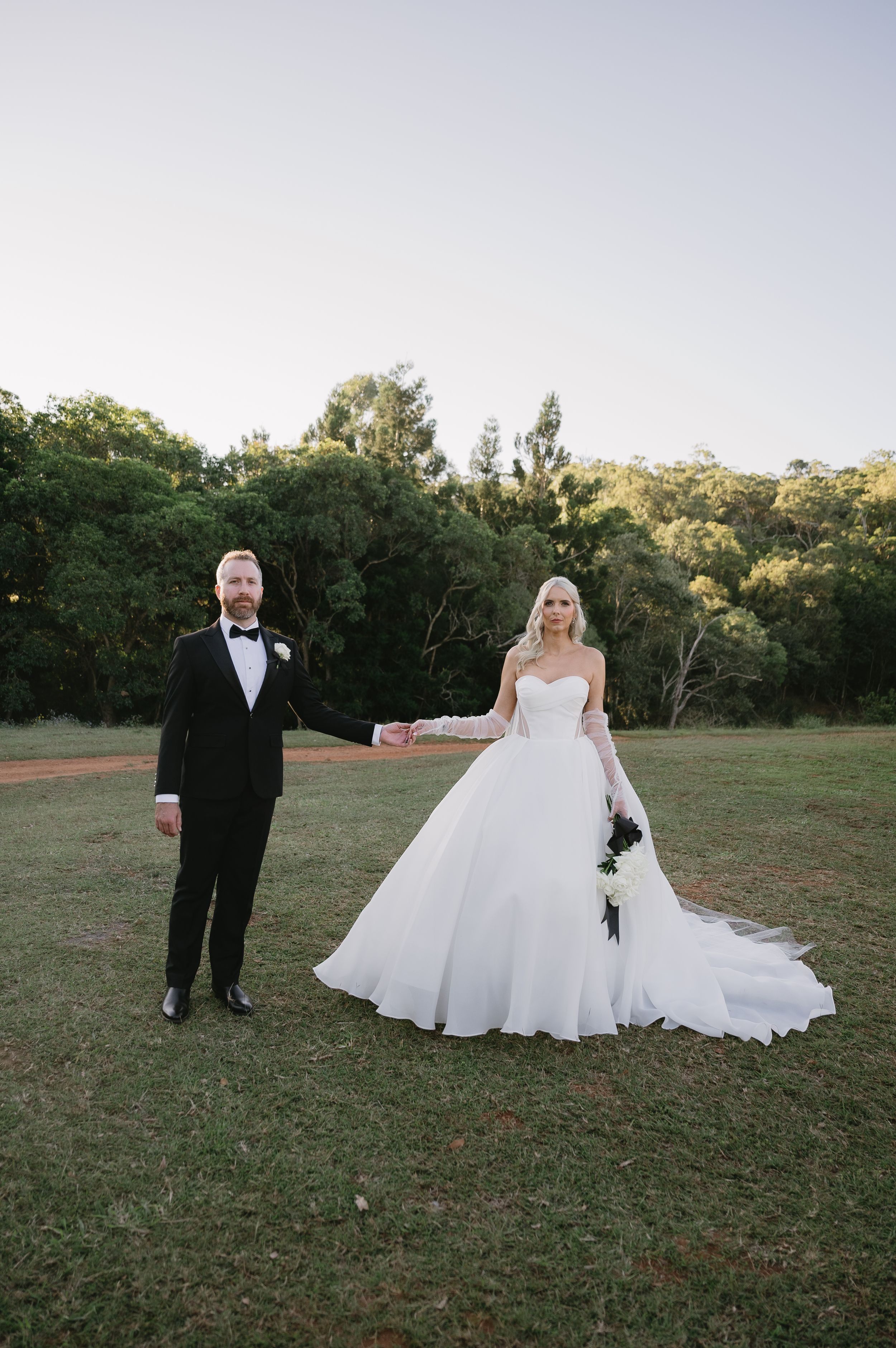 A wedding couple poses in a grassy field during an outdoor photo session at sunset.