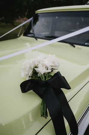 White floral bouquets with black ribbons arranged on a vintage cream-colored car.