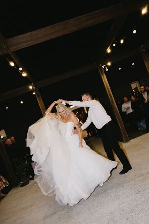 A couple performs an elegant dance move during their first dance at a wedding reception under string lights.