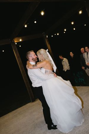 A newlywed couple shares a romantic dance moment on their wedding day beneath wooden beams and twinkle lights.