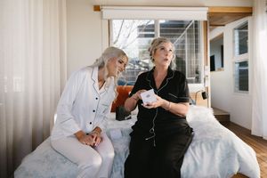 Two people sharing tea and conversation while sitting on a bed in morning light.