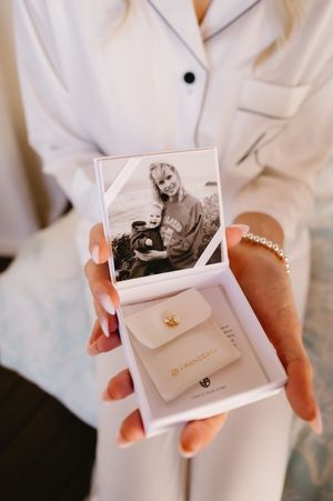 Hands in white sleeves hold a small photo and white envelope with gold details.