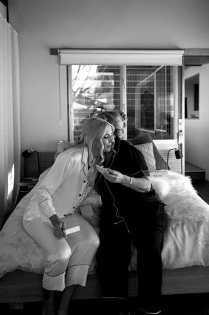 A black and white candid moment shows a couple sharing laughter while getting ready.