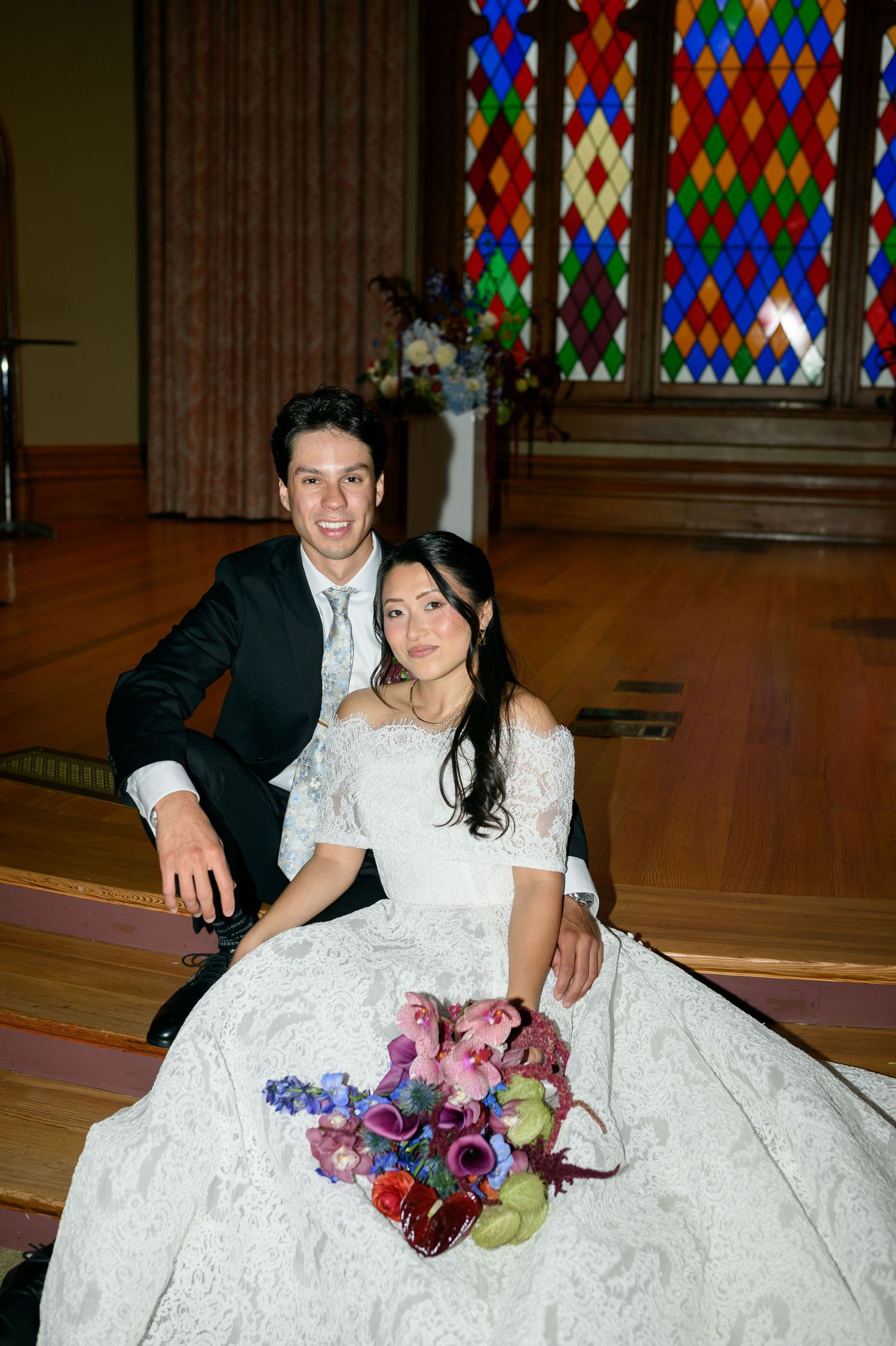 A wedding party holds colorful floral bouquets featuring bright orange, pink and yellow blooms against formal attire.