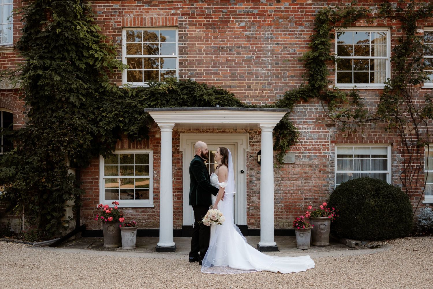 A couple shares a romantic moment against a rustic brick wall at a historic estate venue.