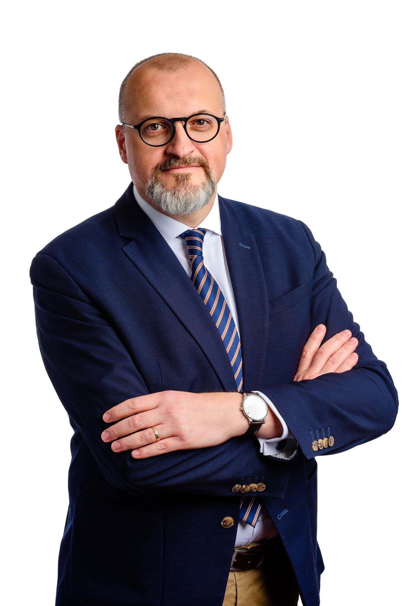 Professional headshot of a person in a navy suit and striped tie wearing glasses with arms crossed against white background.