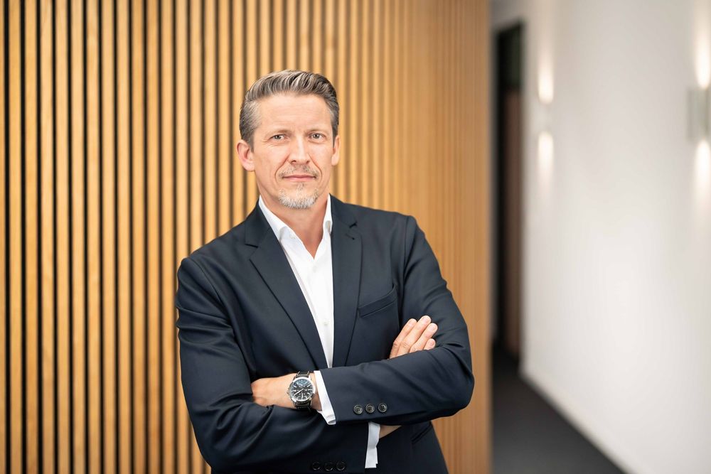 Professional portrait of person in business attire against wooden slat wall in modern office setting.