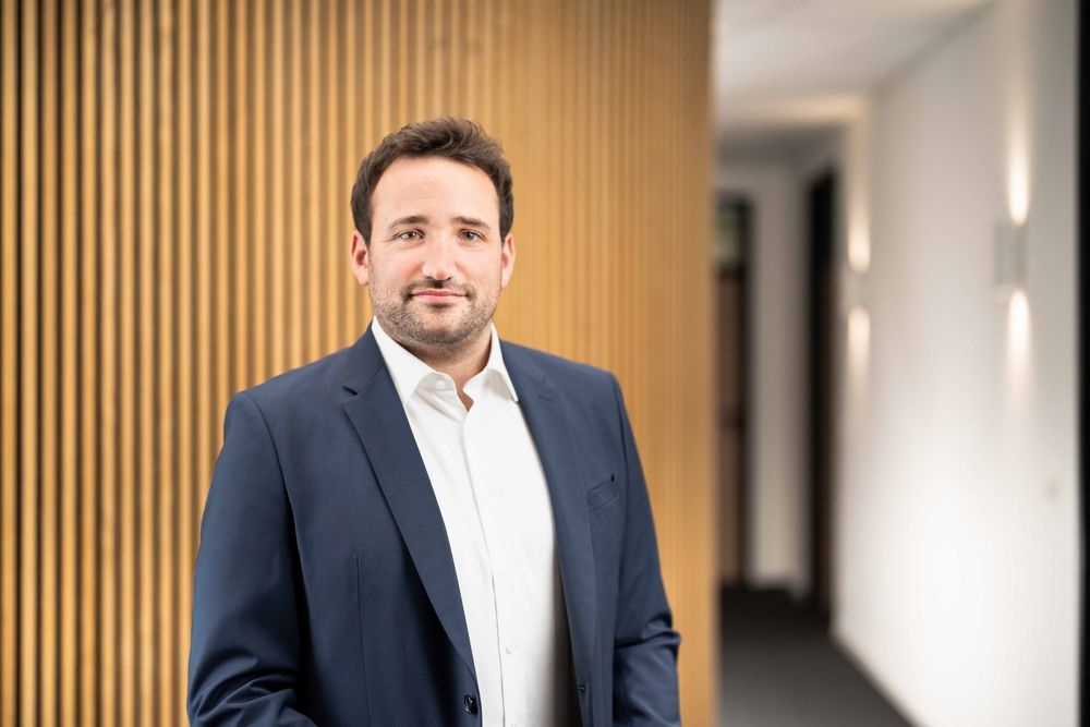 Business portrait showing a person in formal attire standing against vertical wooden slat wall decor.