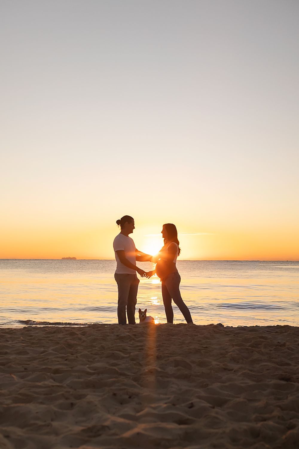 Silhouetted figures stand on a beach at sunset with golden light reflecting off the ocean waves.