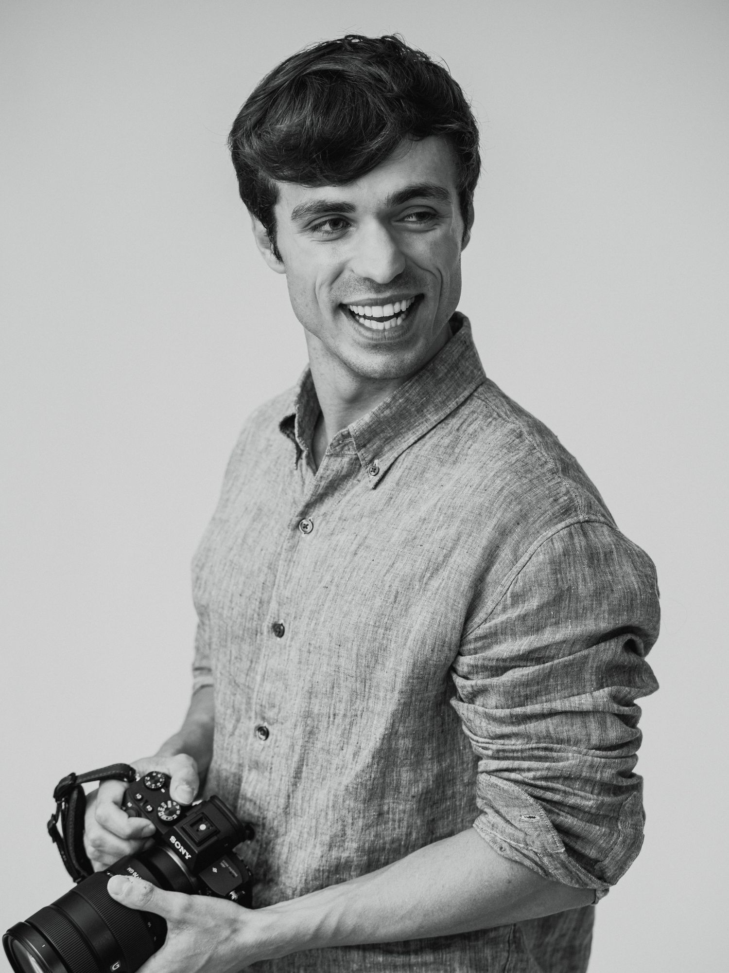 Black and white portrait of a smiling photographer in a linen button-down shirt holding a camera.